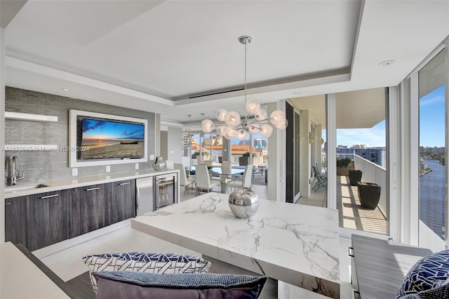 dining area with floor to ceiling windows, a raised ceiling, wine cooler, a notable chandelier, and sink