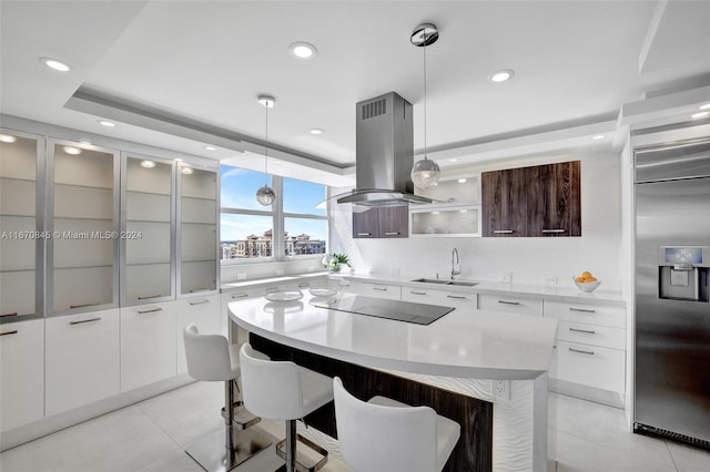 kitchen featuring high quality fridge, a kitchen island, island range hood, hanging light fixtures, and black electric stovetop