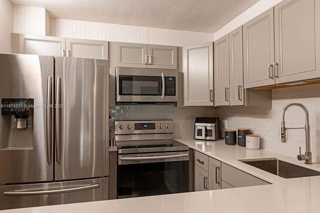 kitchen with decorative backsplash, gray cabinets, stainless steel appliances, light countertops, and a sink