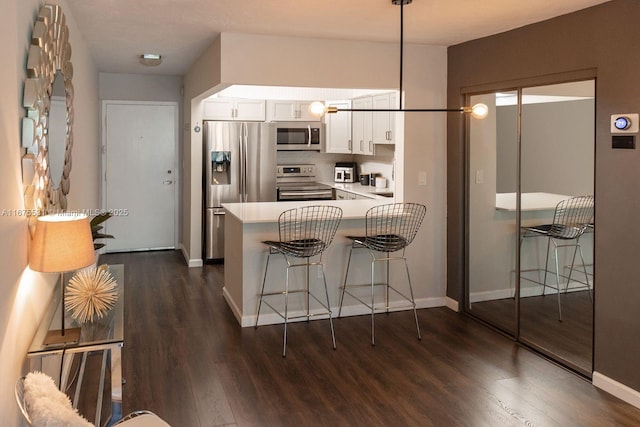 kitchen featuring a peninsula, hanging light fixtures, stainless steel appliances, light countertops, and white cabinetry