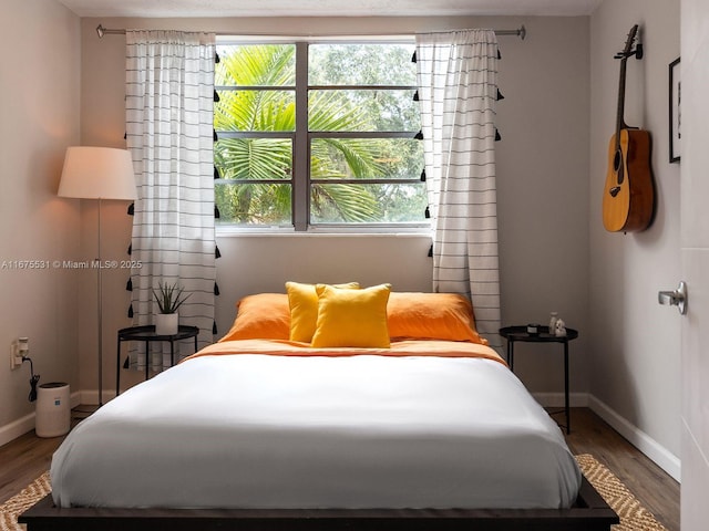 bedroom with multiple windows, baseboards, and wood finished floors