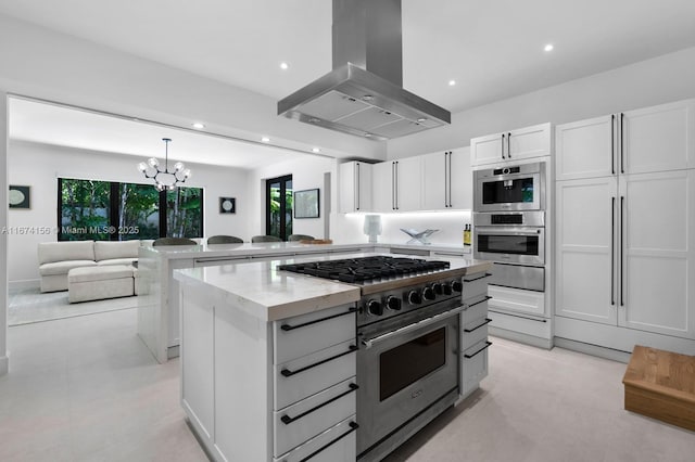 kitchen featuring a kitchen island, appliances with stainless steel finishes, island range hood, white cabinetry, and kitchen peninsula