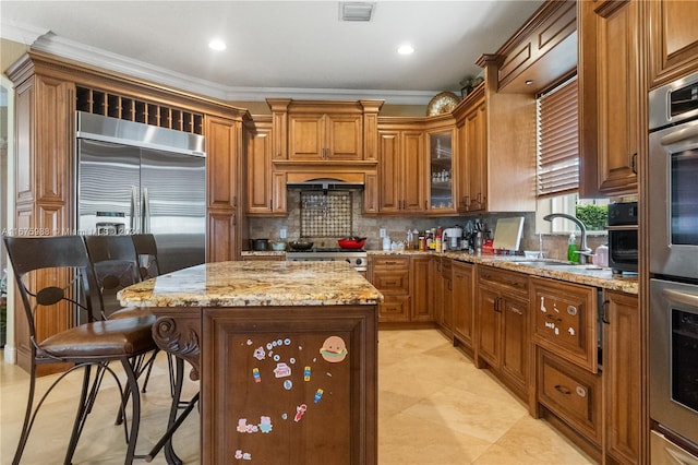 kitchen with light stone countertops, appliances with stainless steel finishes, a center island, a kitchen breakfast bar, and ornamental molding