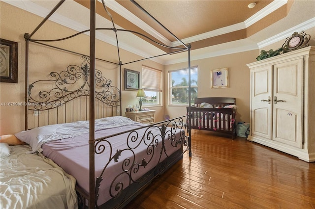 bedroom with dark wood-type flooring, crown molding, and a tray ceiling