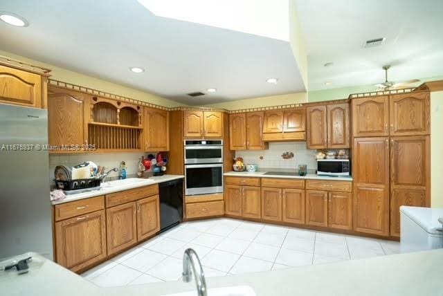 kitchen with tasteful backsplash, sink, light tile patterned floors, and black appliances