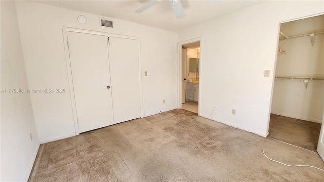 unfurnished bedroom with ceiling fan, light colored carpet, connected bathroom, and multiple closets