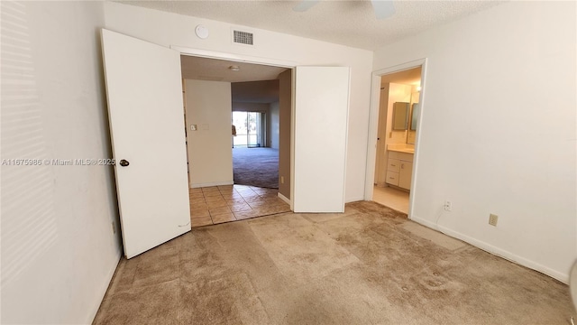 unfurnished bedroom featuring light carpet, ceiling fan, ensuite bathroom, and a textured ceiling