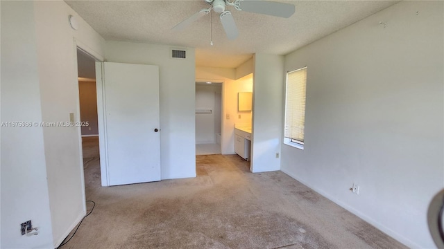 unfurnished bedroom with a textured ceiling, ceiling fan, light colored carpet, and ensuite bathroom