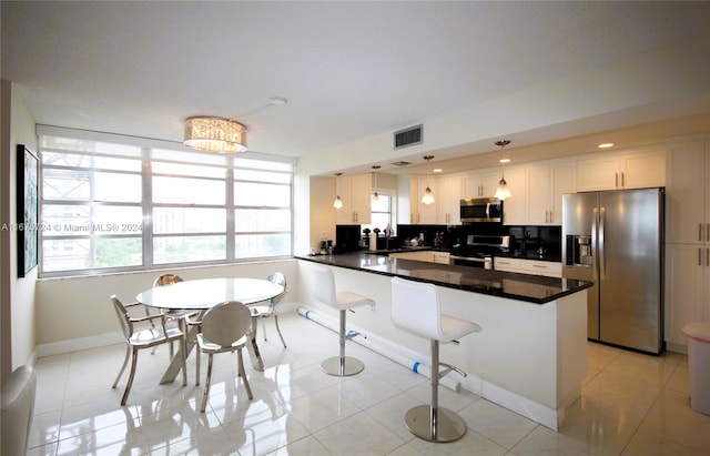 kitchen with plenty of natural light, decorative light fixtures, kitchen peninsula, appliances with stainless steel finishes, and white cabinetry