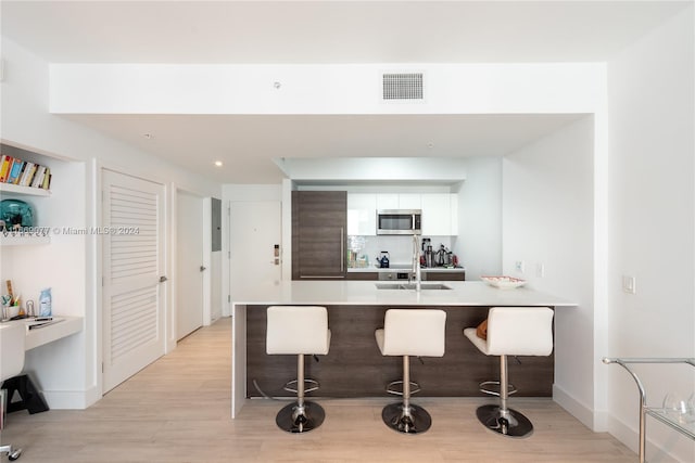 kitchen with light wood-type flooring, white cabinets, sink, kitchen peninsula, and a breakfast bar area