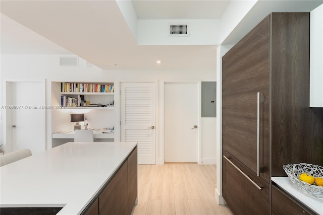 kitchen featuring electric panel, light hardwood / wood-style flooring, and dark brown cabinets