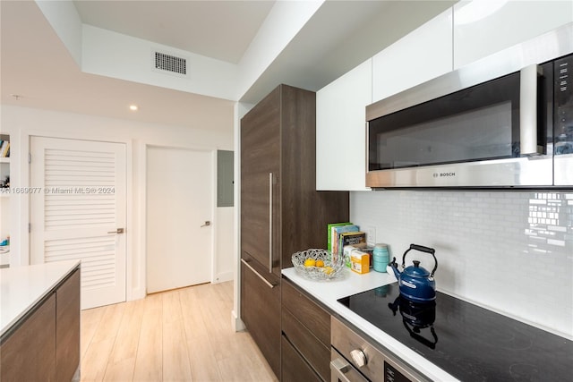 kitchen with dark brown cabinetry, wall oven, tasteful backsplash, white cabinetry, and light wood-type flooring