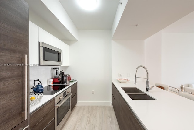 kitchen with light wood-type flooring, dark brown cabinetry, sink, white cabinets, and appliances with stainless steel finishes