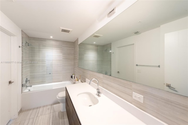 full bathroom with vanity, tiled shower / bath combo, tile patterned floors, tile walls, and toilet