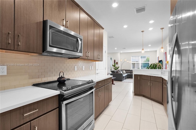 kitchen featuring sink, tasteful backsplash, dark brown cabinets, hanging light fixtures, and appliances with stainless steel finishes