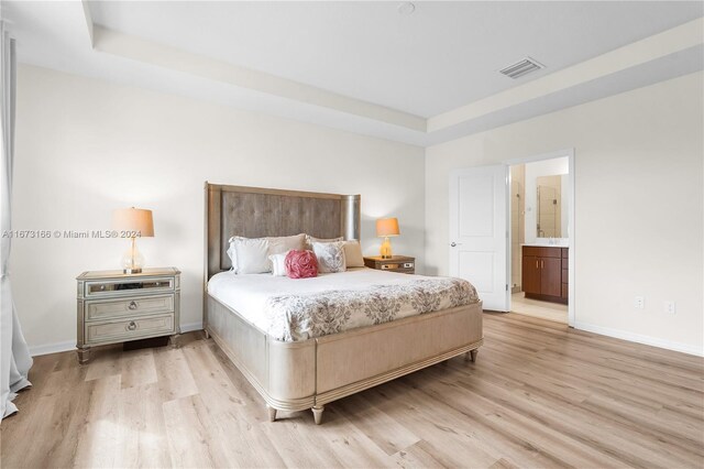 bedroom with connected bathroom, a tray ceiling, and light wood-type flooring