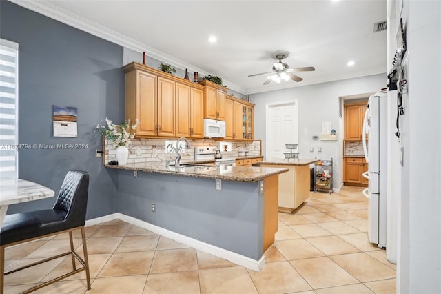 kitchen with white appliances, stone countertops, a breakfast bar, and kitchen peninsula