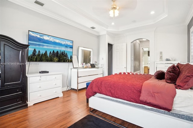 bedroom with ensuite bathroom, ornamental molding, ceiling fan, a tray ceiling, and light hardwood / wood-style flooring