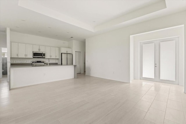 kitchen with a raised ceiling, french doors, white cabinets, and appliances with stainless steel finishes