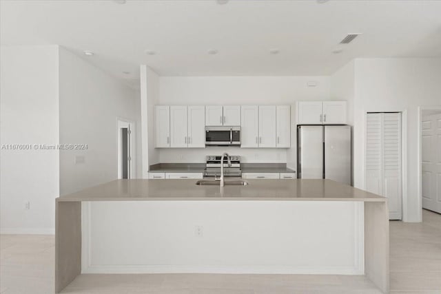 kitchen with appliances with stainless steel finishes, white cabinetry, and an island with sink