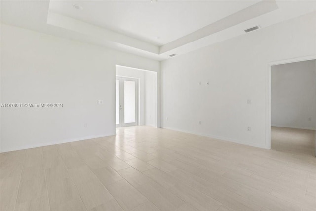 unfurnished room featuring french doors, a tray ceiling, and light wood-type flooring