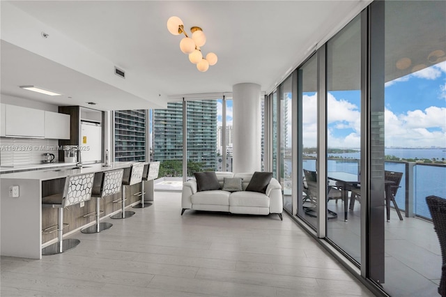 living room with light wood-type flooring, a water view, and a wall of windows