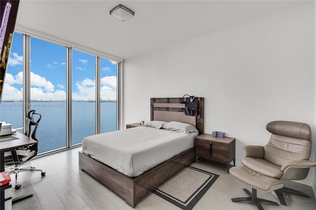 bedroom with access to exterior, wood-type flooring, a water view, and floor to ceiling windows