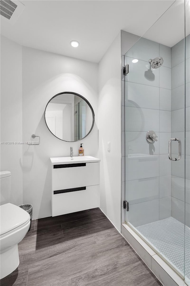 bathroom featuring hardwood / wood-style floors, vanity, toilet, and a shower with door