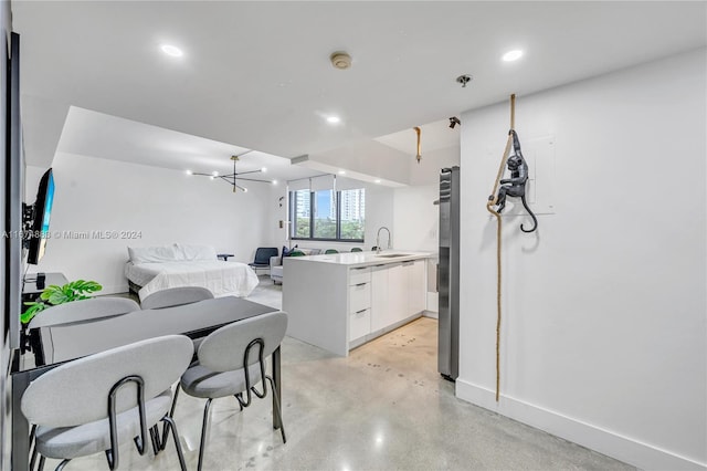 kitchen featuring white cabinets, stainless steel fridge, sink, kitchen peninsula, and a notable chandelier