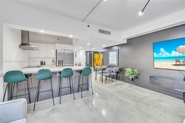 kitchen featuring stainless steel fridge with ice dispenser, wall chimney range hood, white cabinetry, and a breakfast bar