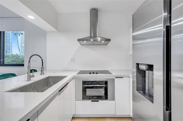 kitchen with black appliances, wall chimney range hood, white cabinetry, and sink