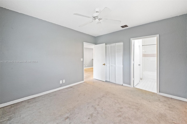 unfurnished bedroom featuring a closet, light carpet, ensuite bathroom, and ceiling fan