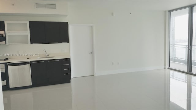 kitchen with a sink, dark cabinetry, stainless steel dishwasher, a wall of windows, and plenty of natural light