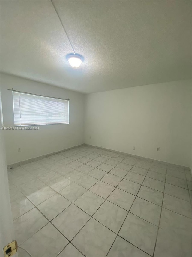 empty room with light tile patterned flooring and a textured ceiling