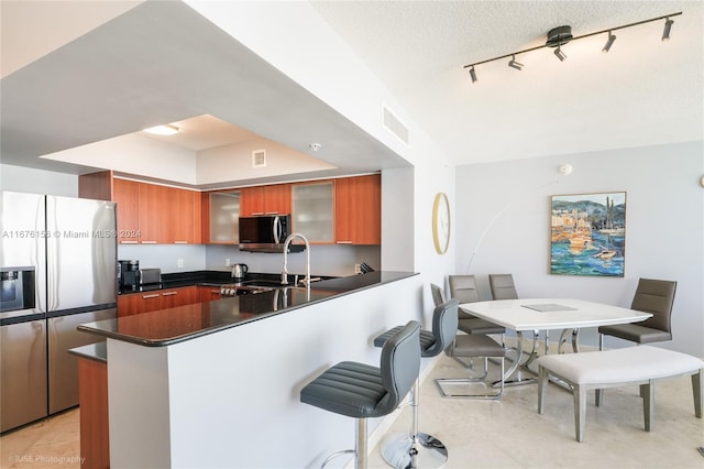 kitchen featuring a breakfast bar area, sink, kitchen peninsula, appliances with stainless steel finishes, and a textured ceiling