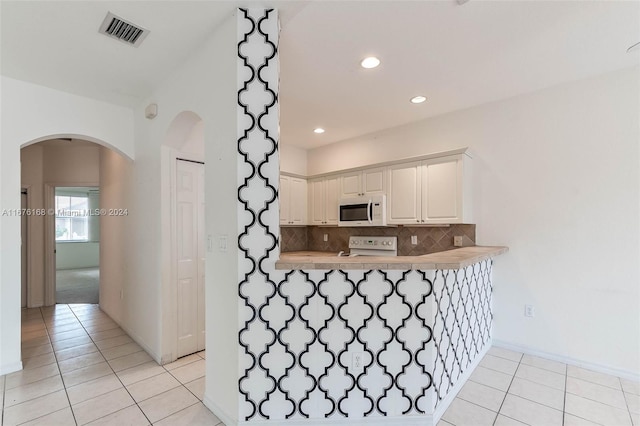 kitchen with white appliances, tasteful backsplash, kitchen peninsula, white cabinets, and light tile patterned floors