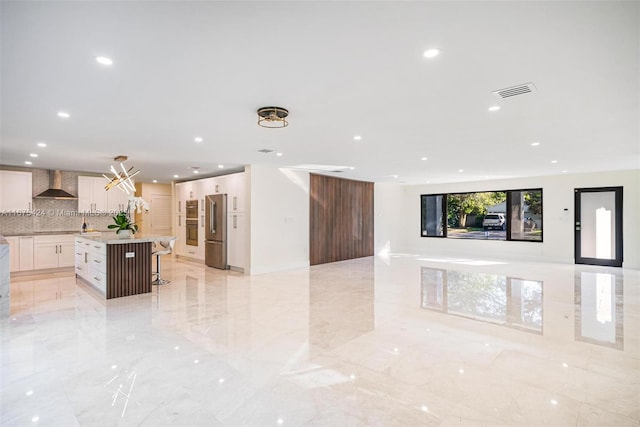 kitchen featuring white cabinets, a large island, a breakfast bar area, open floor plan, and wall chimney range hood