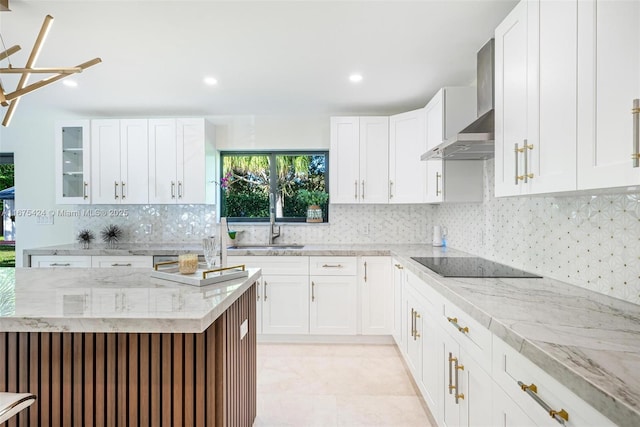 kitchen with glass insert cabinets, black electric cooktop, wall chimney range hood, white cabinetry, and a sink