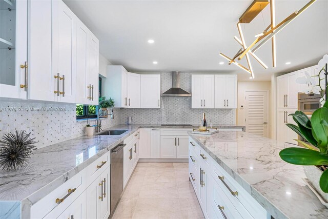 kitchen featuring pendant lighting, stainless steel dishwasher, white cabinets, a sink, and wall chimney range hood