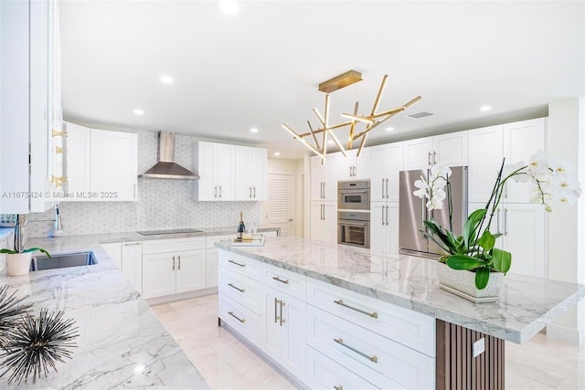 kitchen with white cabinets, a center island, light stone countertops, stainless steel appliances, and wall chimney range hood