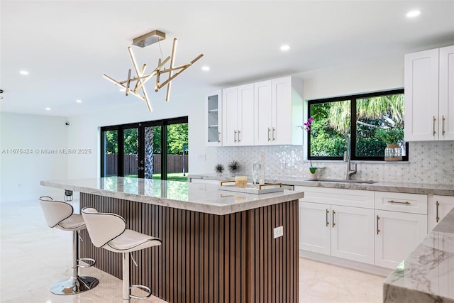 kitchen with light stone counters, glass insert cabinets, a sink, and white cabinetry