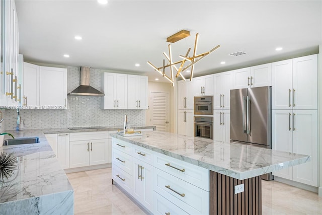 kitchen with light stone counters, white cabinets, a sink, a kitchen island, and wall chimney exhaust hood