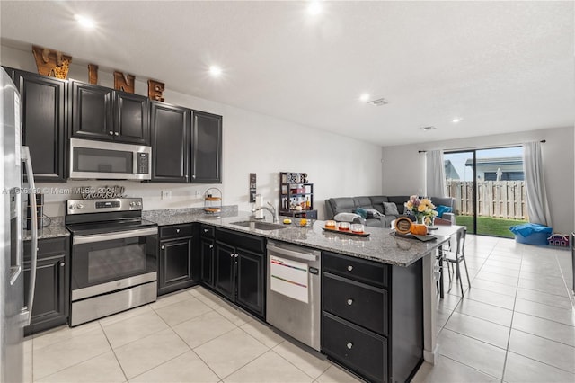 kitchen with light tile patterned flooring, light stone countertops, sink, kitchen peninsula, and appliances with stainless steel finishes