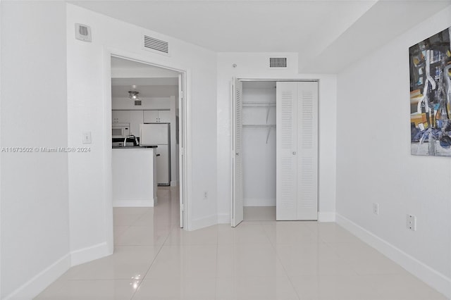 unfurnished bedroom featuring light tile patterned flooring, white refrigerator, and a closet