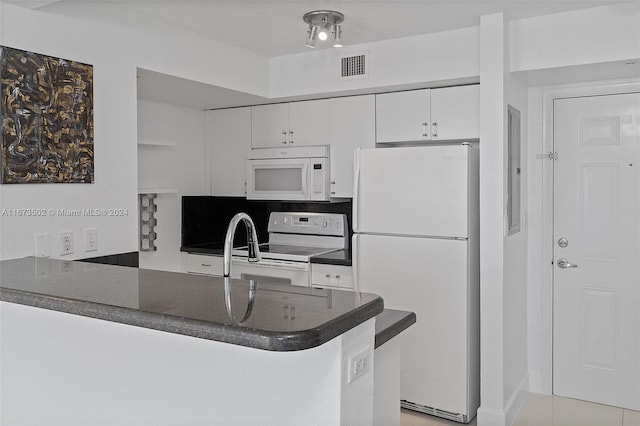 kitchen with kitchen peninsula, sink, light tile patterned floors, white cabinetry, and white appliances