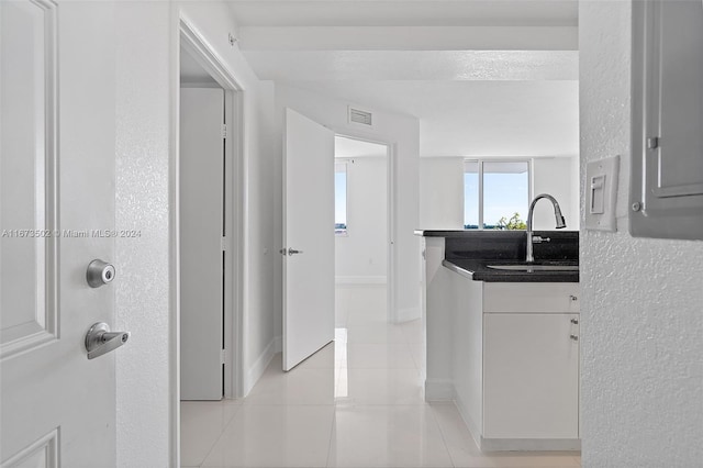 interior space with a textured ceiling, sink, light tile patterned flooring, and white cabinets