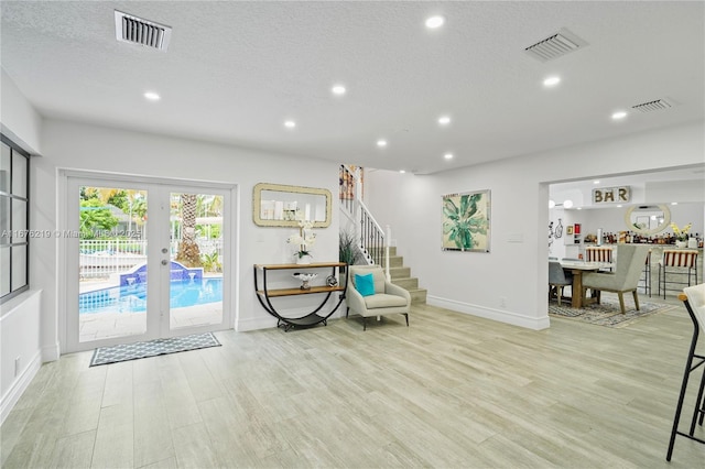 living area with a textured ceiling, light hardwood / wood-style floors, and french doors