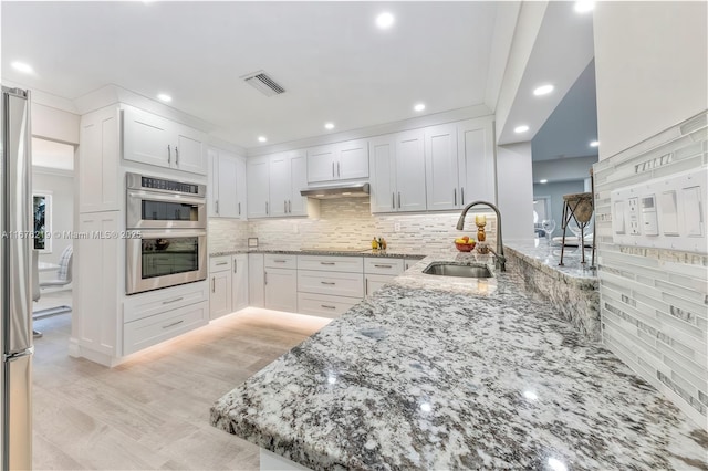 kitchen featuring white cabinetry, sink, light stone countertops, and kitchen peninsula