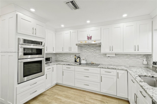 kitchen with black electric cooktop, stainless steel double oven, white cabinetry, and light hardwood / wood-style floors