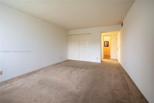 unfurnished bedroom with a textured ceiling, a closet, and light colored carpet
